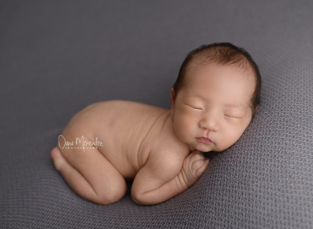Baby sleeping peacefully on a soft gray blanket.