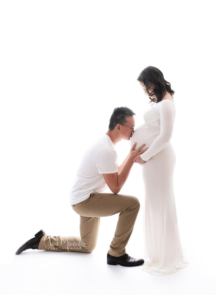 Expecting couple with partner kneeling and touching pregnant belly.
