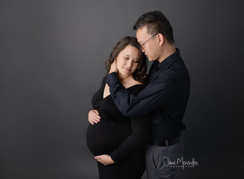 Pregnant woman and partner embracing, celebrating pregnancy in a studio setting.