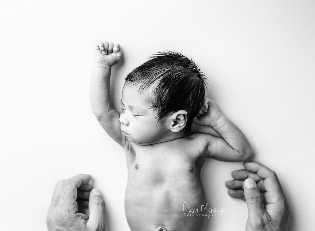Newborn baby peacefully sleeping with hands near face, captured in black and white.