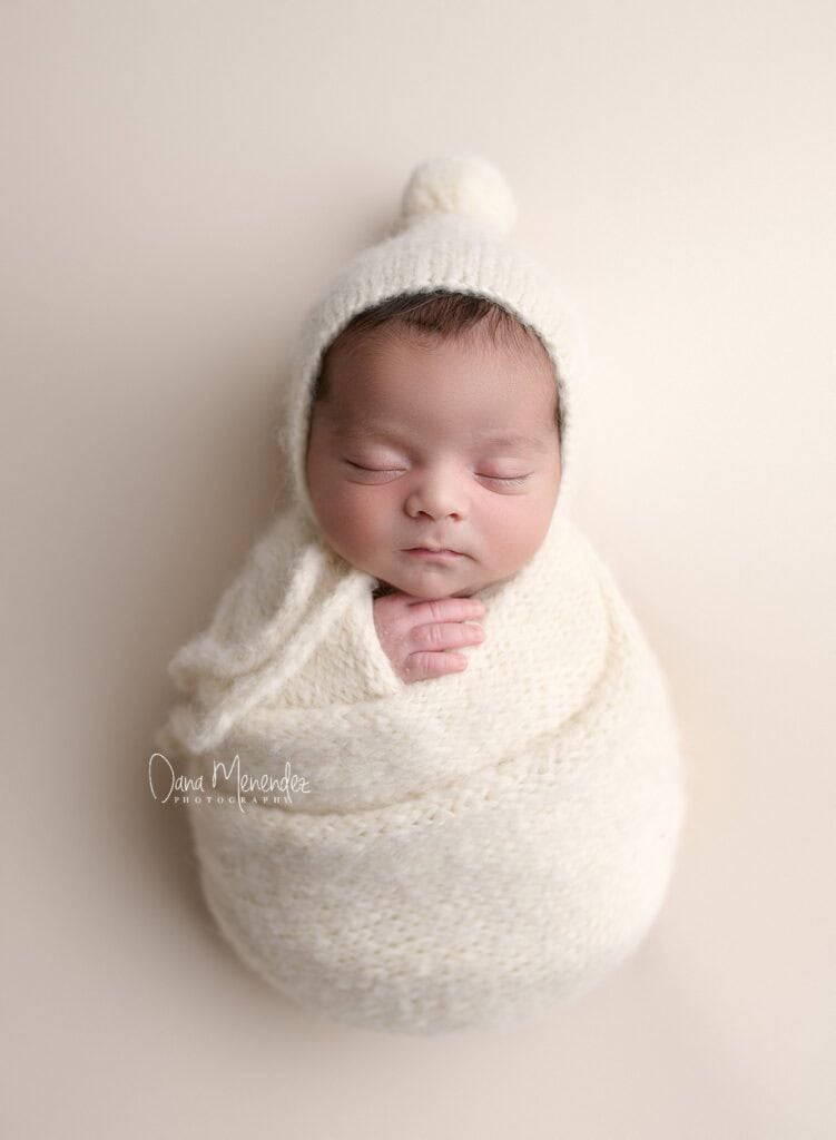 Baby sleeping peacefully in a cozy cream swaddle and hat.