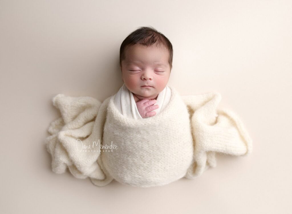 Newborn baby peacefully sleeping wrapped in a cream blanket.