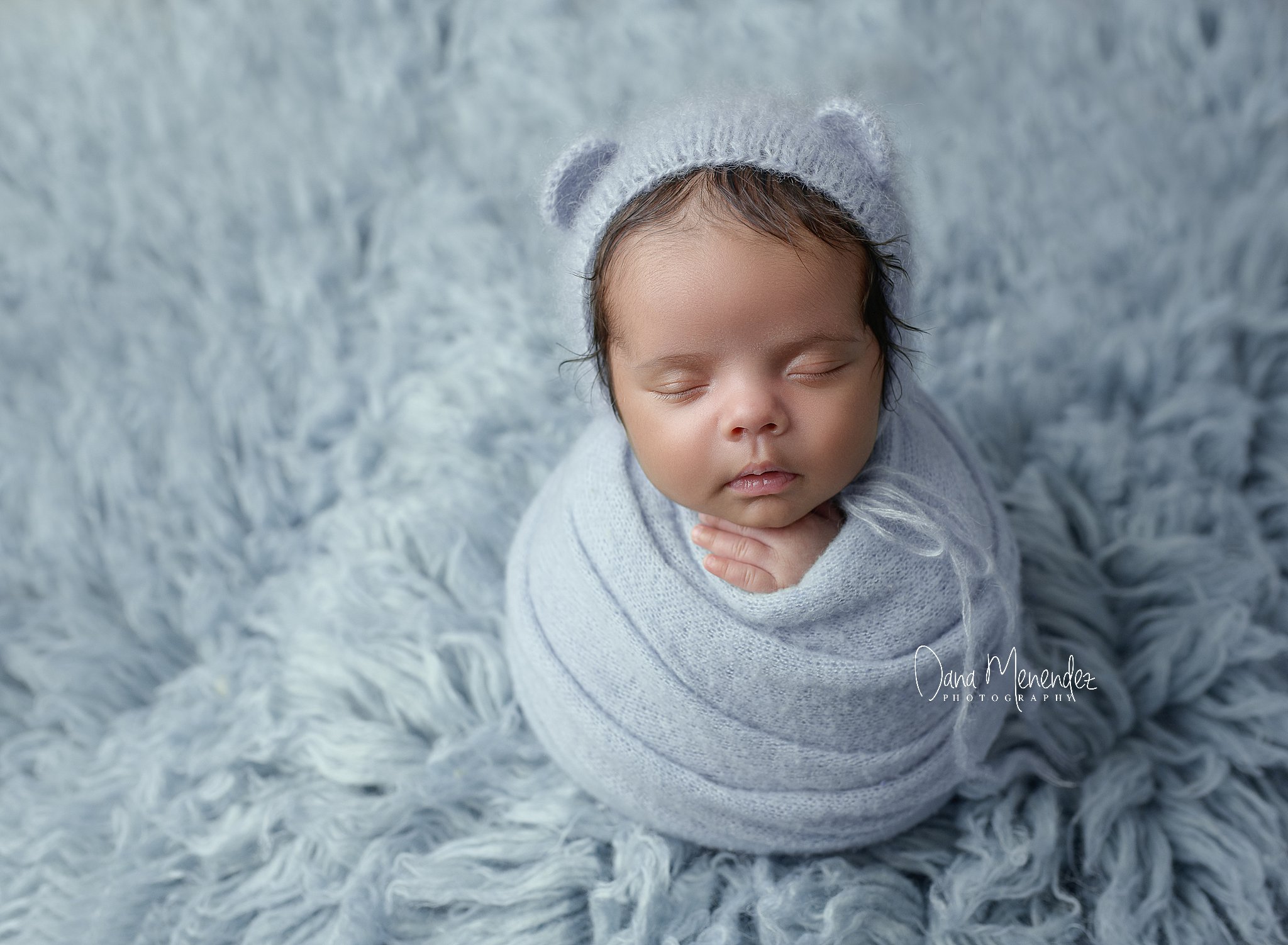 Baby sleeping wrapped in gray with bear hat.