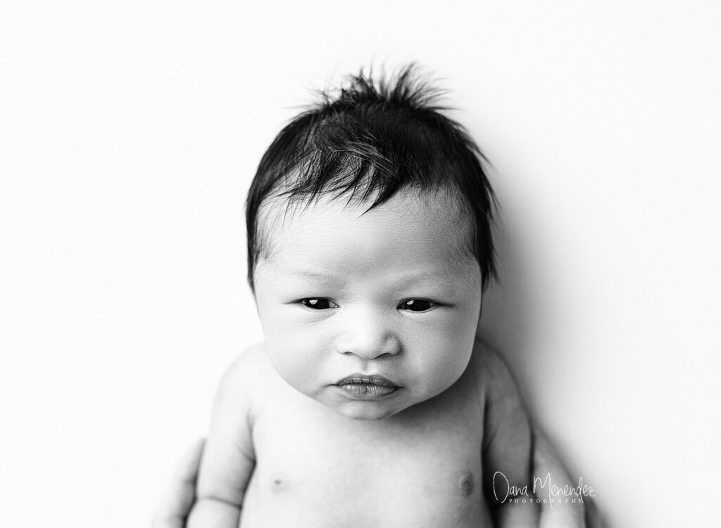 Baby portrait of a newborn with a serious expression, black and white photography.