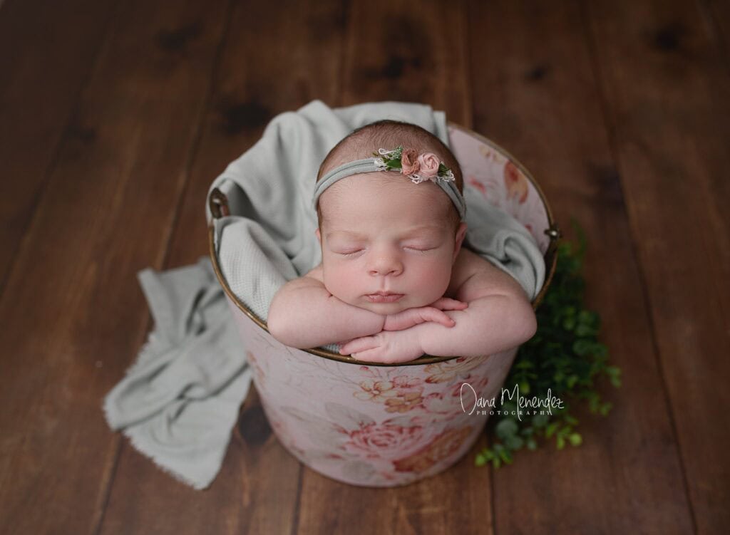 Adorable newborn sleeping in a floral basket with a headband.