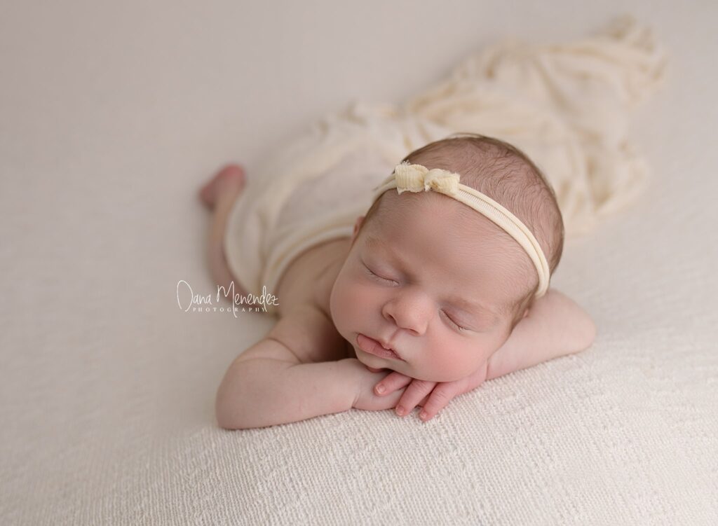 Baby sleeping peacefully on cream blanket with headband.