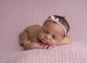 Baby girl peacefully sleeping on pink textured blanket with a pink headband.