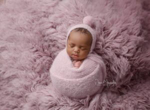 Baby girl peacefully sleeping wrapped in pink blanket.