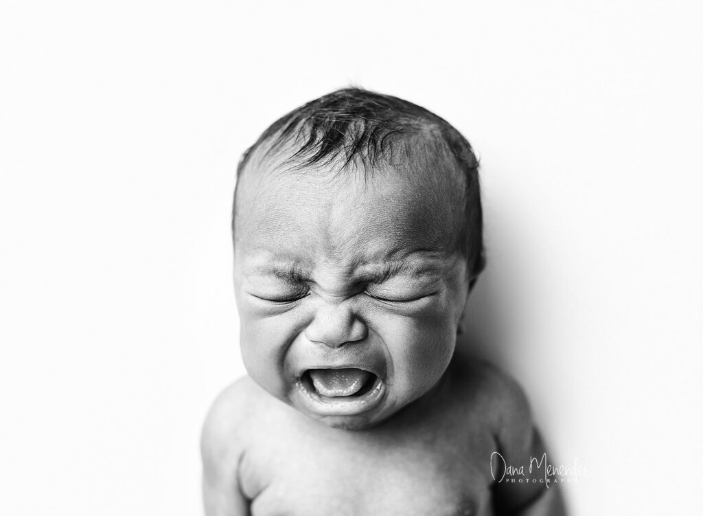 Newborn baby crying, black and white portrait, emotional expression.