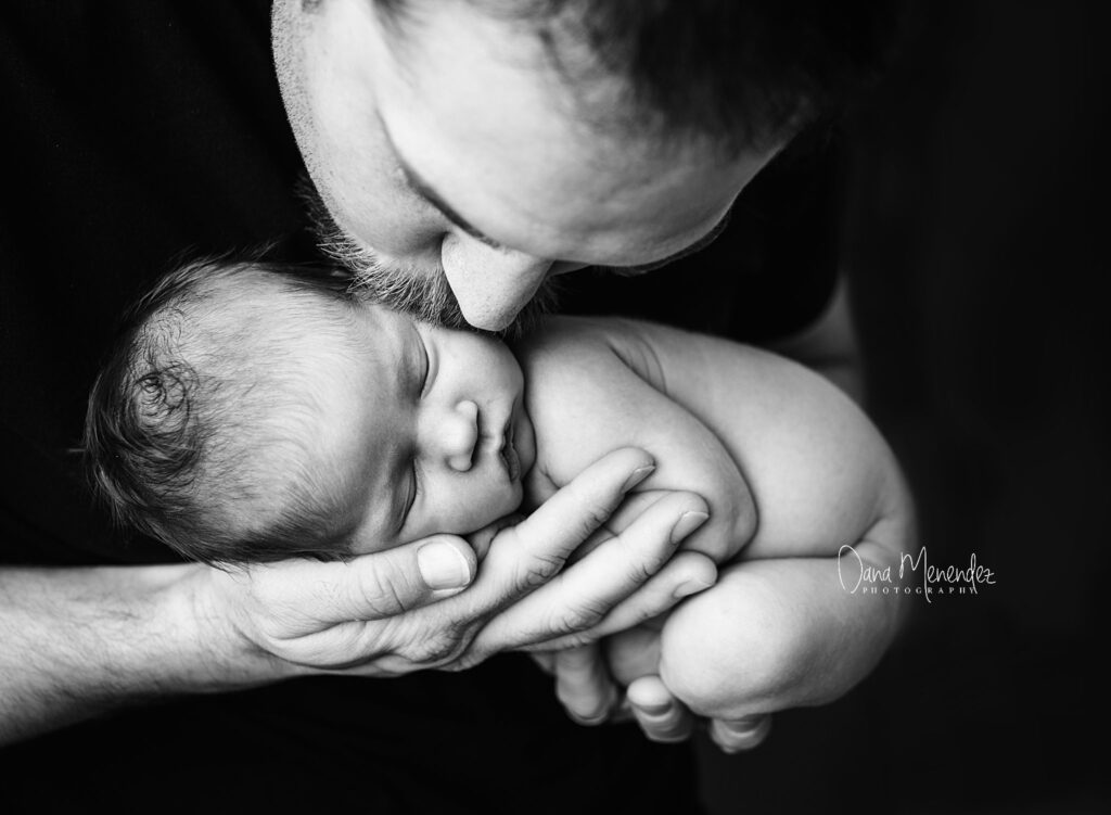 Father gently holding newborn baby, close-up black and white photo.