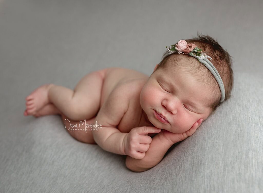 Baby sleeping peacefully on gray blanket with floral headband.