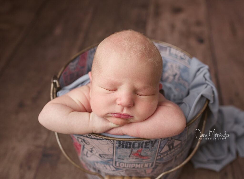 Newborn baby sleeping in a decorative basket with a hockey theme.