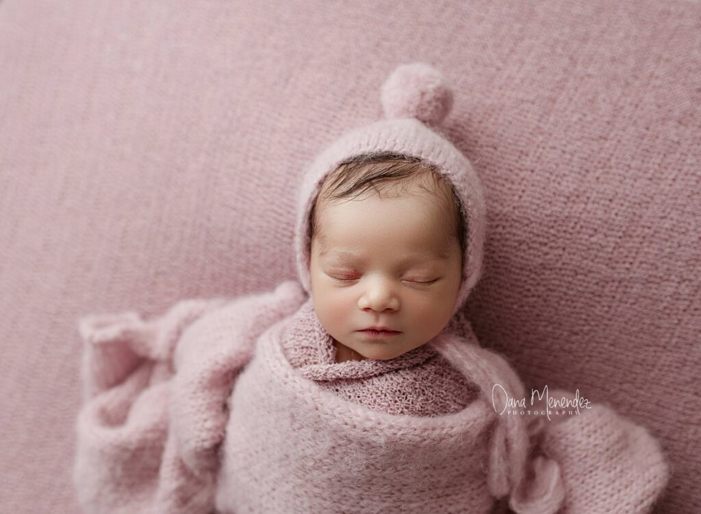 Adorable newborn baby wrapped in pink blanket and hat, sleeping peacefully.