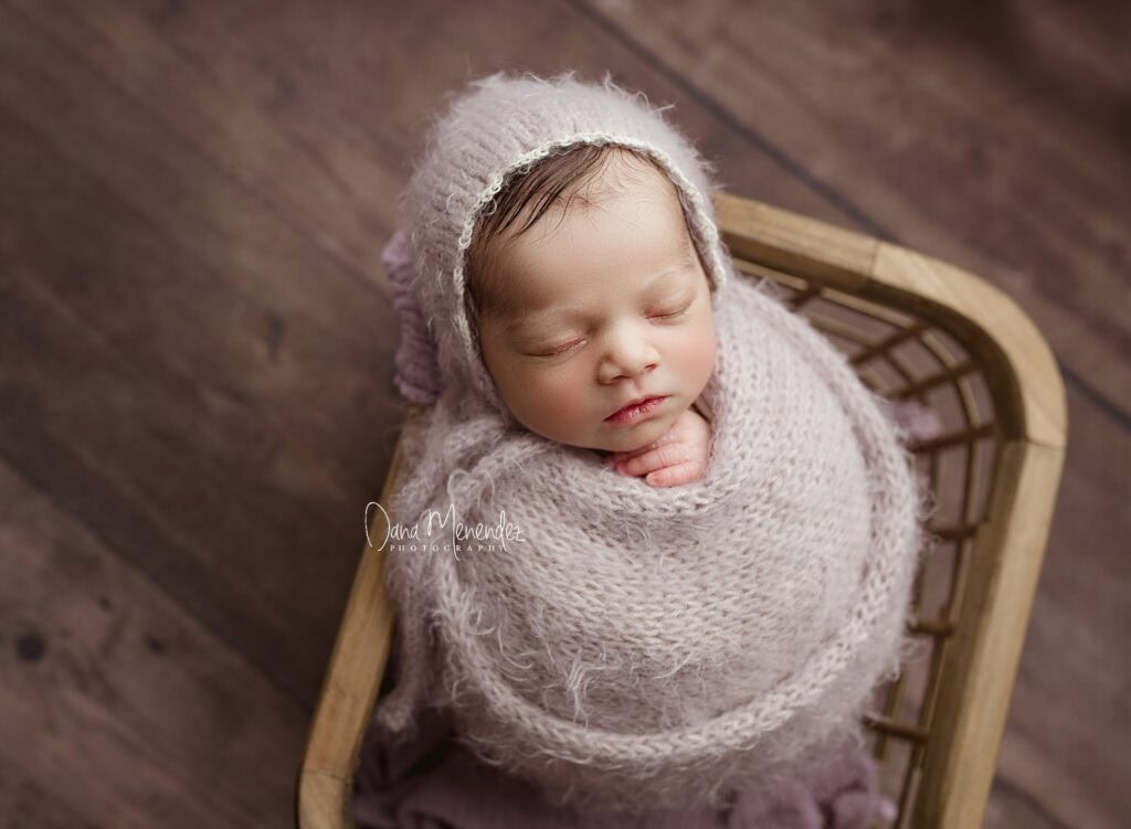 Adorable newborn baby wrapped in soft knit blanket and bonnet, sleeping peacefully.
