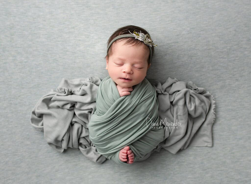 Adorable newborn baby wrapped in green swaddle with floral headband.