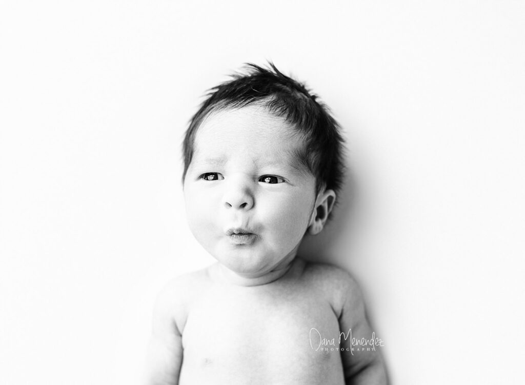 Baby portrait of a newborn with a curious expression, captured in black and white.