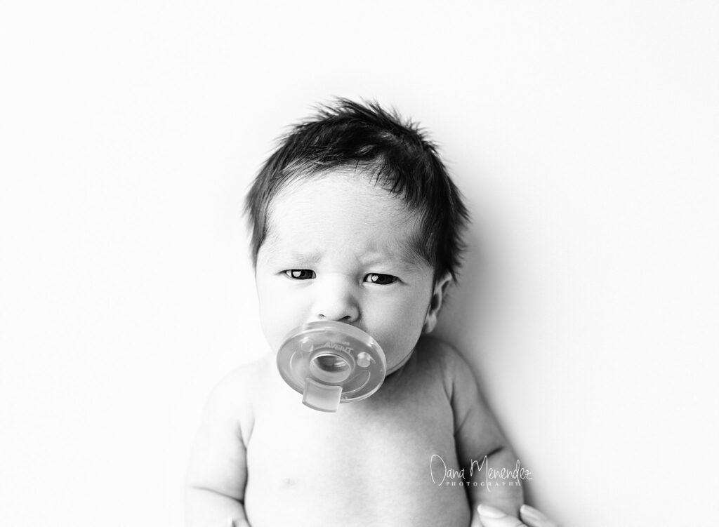 Newborn baby with pacifier, black and white photo.