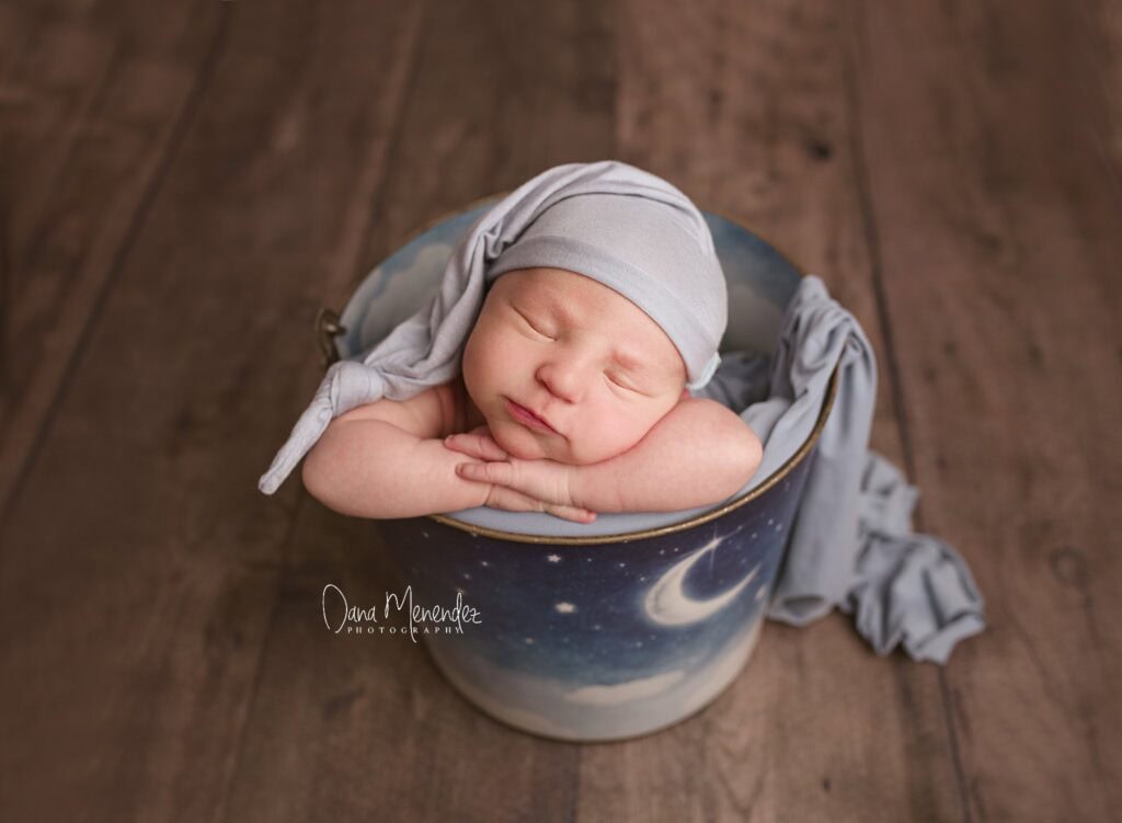 Baby sleeping in moon-themed basket, wrapped in soft gray blanket, during Orion's newborn session.