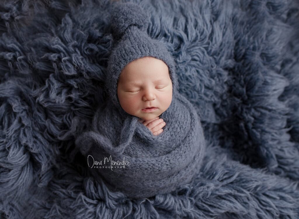 Adorable newborn peacefully sleeping in a soft gray wrap and matching hat, nestled on a plush textur.
