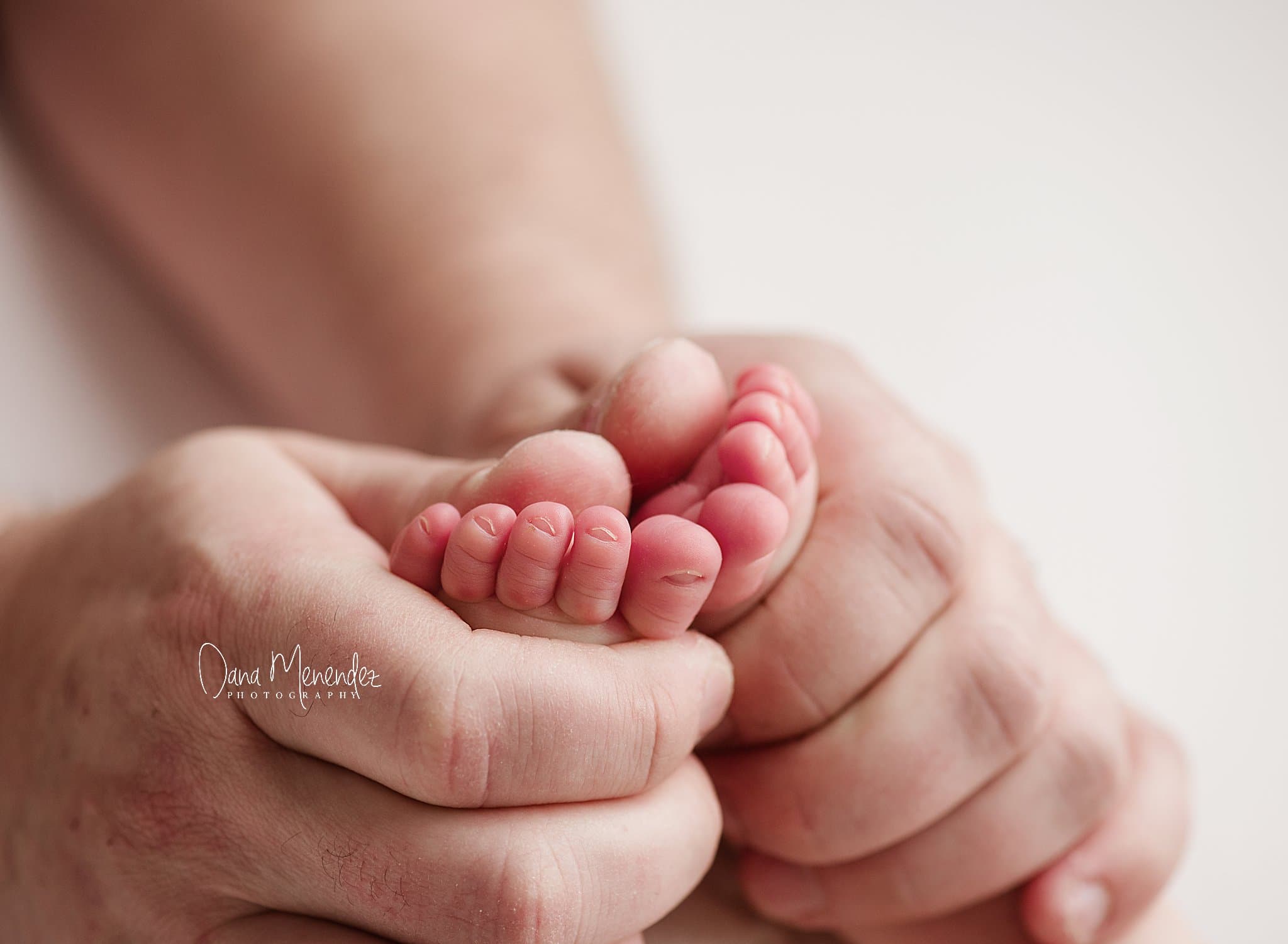 Close-up of a tiny newborn hand held gently by an adult's hand.