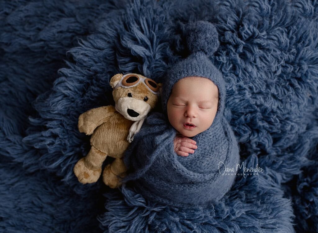 Cute newborn sleeping peacefully in a blue wrap with a plush teddy bear beside him in Calgary AB
