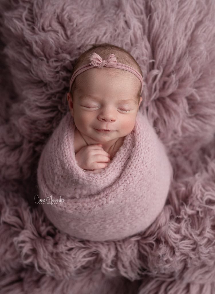 Adorable newborn girl peacefully sleeping in pink wrap on fluffy pink blanket.