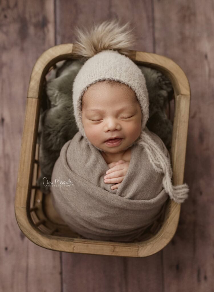 Adorable newborn wrapped in cozy blanket and hat in a wooden basket.