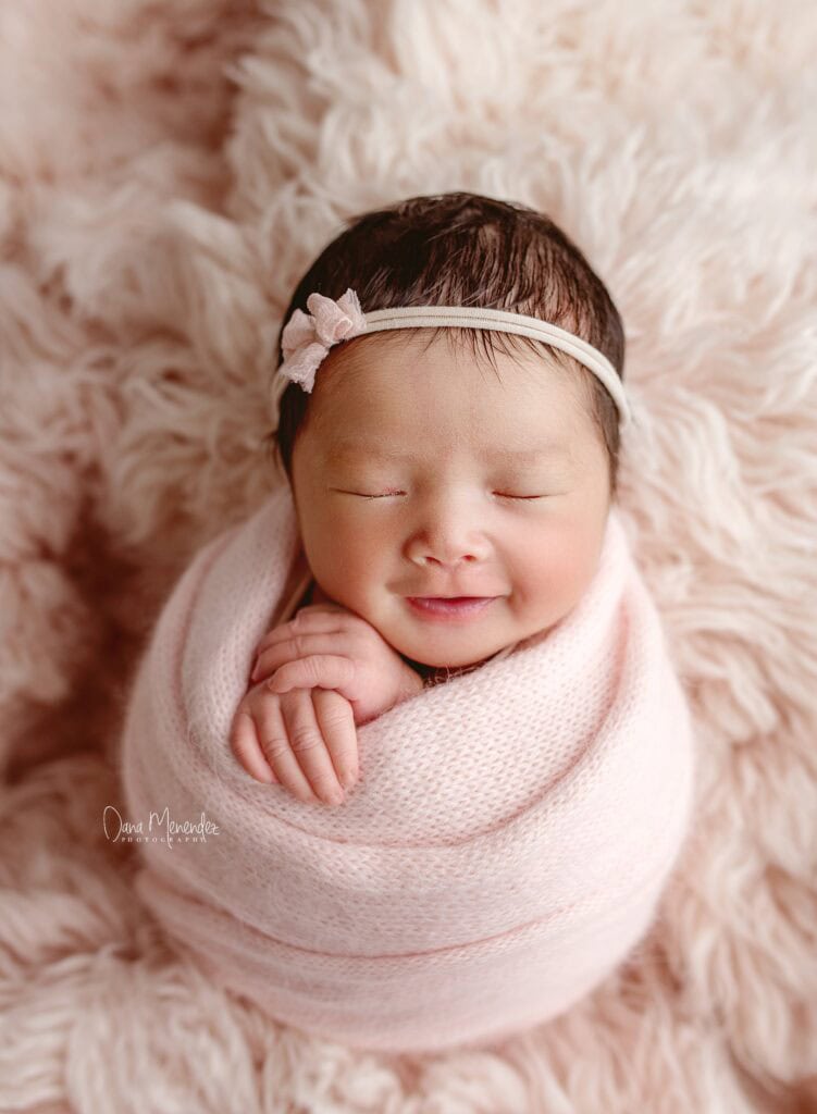 Adorable newborn girl peacefully sleeping in a pink wrap with a headband.