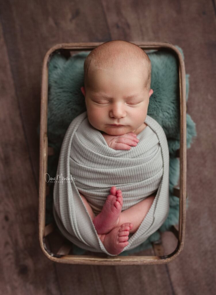 Baby sleeping peacefully in a cozy wooden crate with soft teal blanket.