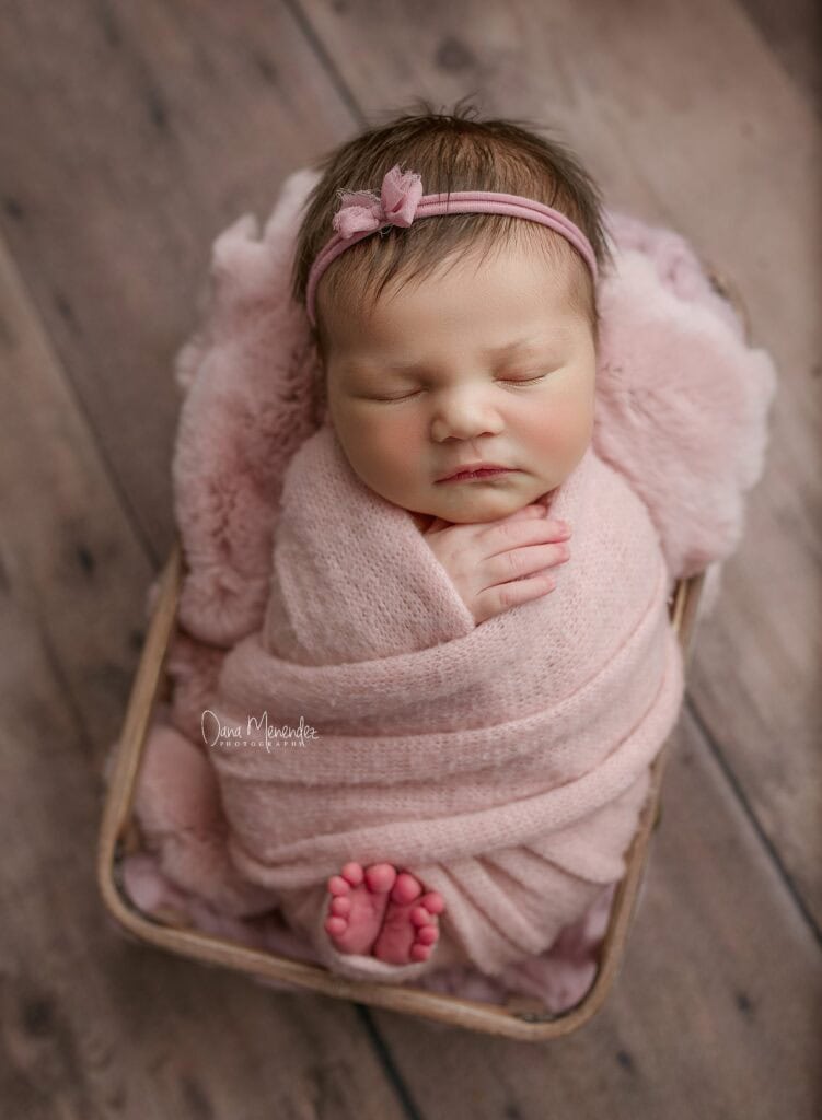 Baby girl peacefully sleeping in pink swaddle with headband.