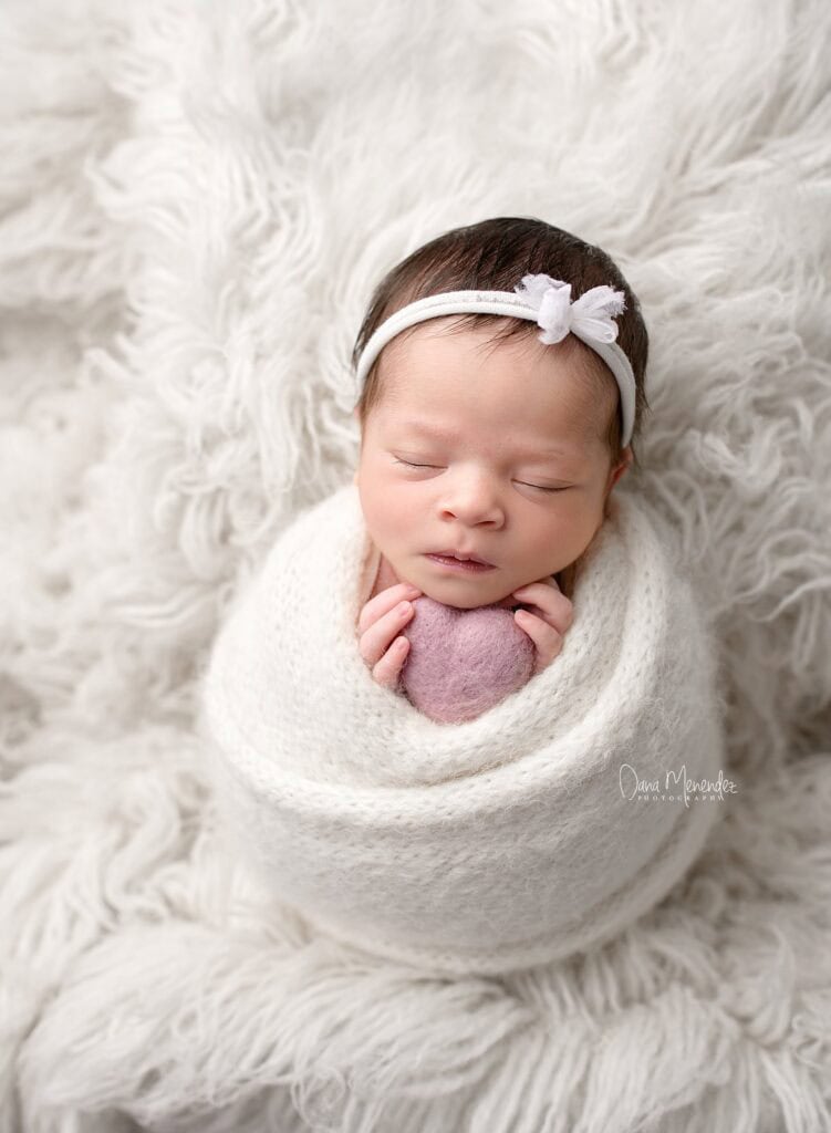 Adorable newborn girl wrapped in a blanket, sleeping peacefully on a fluffy white background.