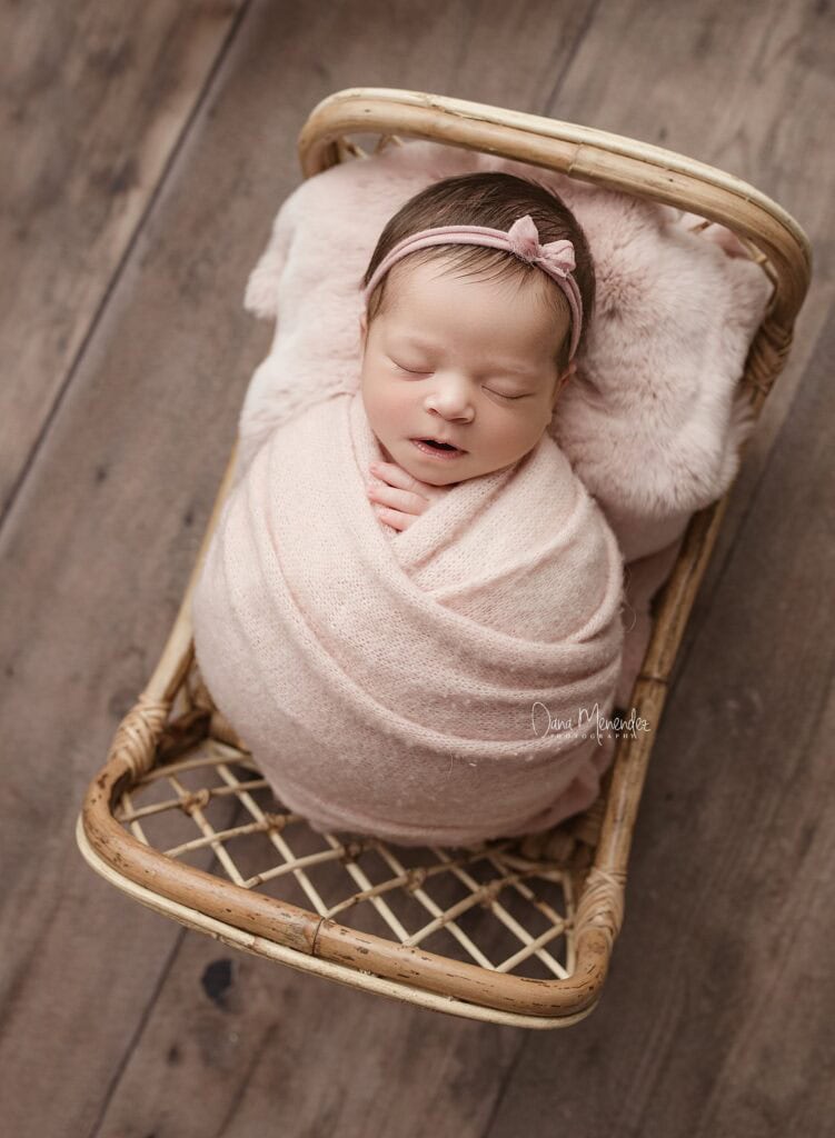 Adorable newborn baby peacefully sleeping in a wicker basket with pink headband.