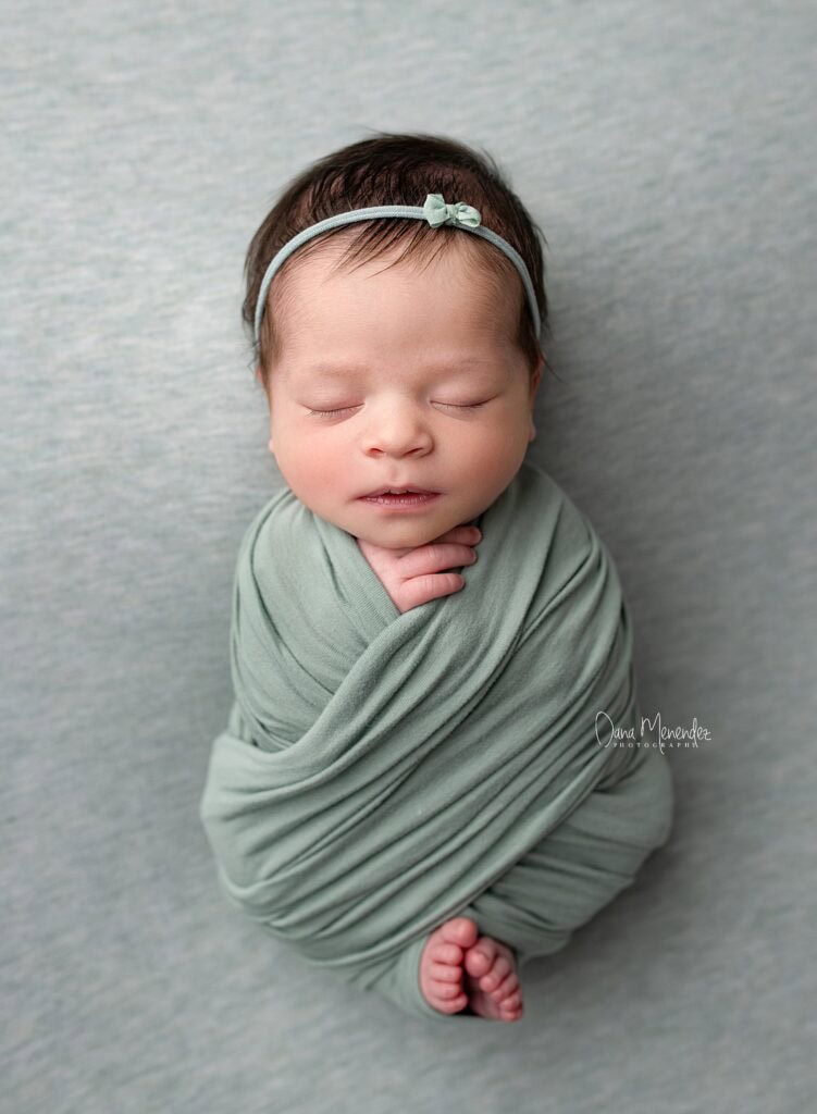 Adorable newborn girl peacefully sleeping, wrapped in a soft green blanket with a matching headband.