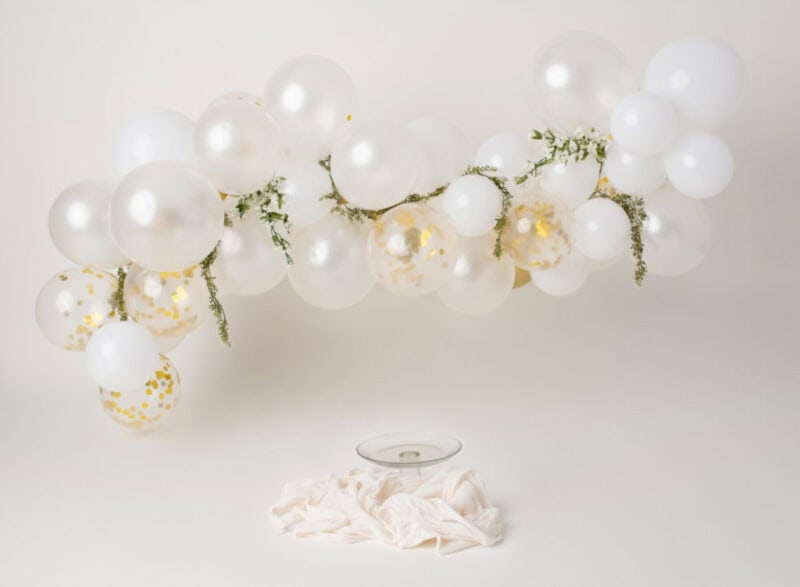 White balloon garland with gold confetti accents for cake smash photoshoot.