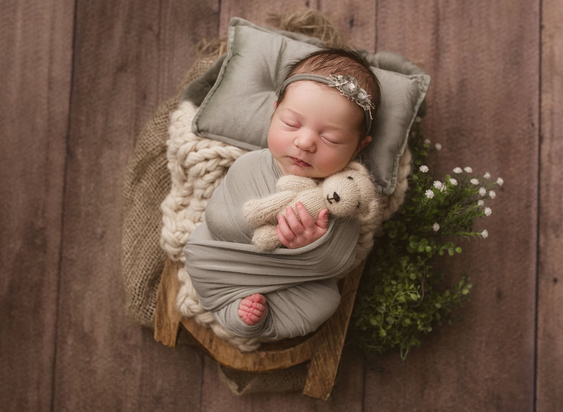 Adorable newborn girl peacefully sleeping, wrapped in a cozy gray blanket with a headband, on a wood in Okotoks