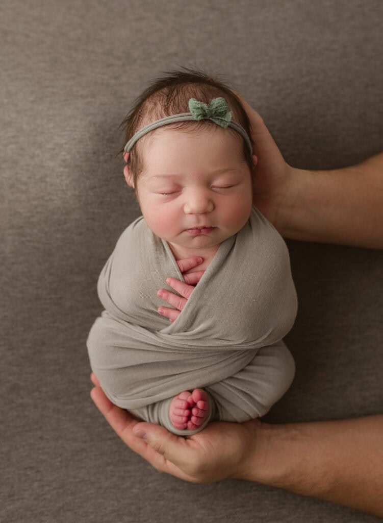 Adorable newborn baby wrapped in gray swaddle with headband, sleeping peacefully.
