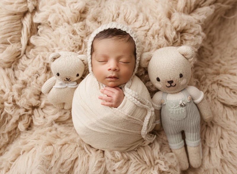 Baby sleeping with stuffed animals on cozy blanket.