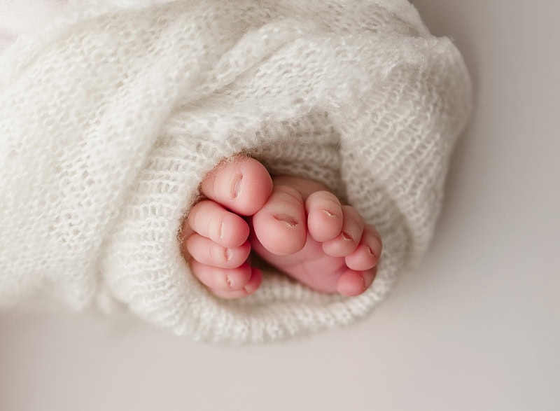Close-up of tiny baby feet wrapped in a cozy white blanket, highlighting delicate skin and curled to.