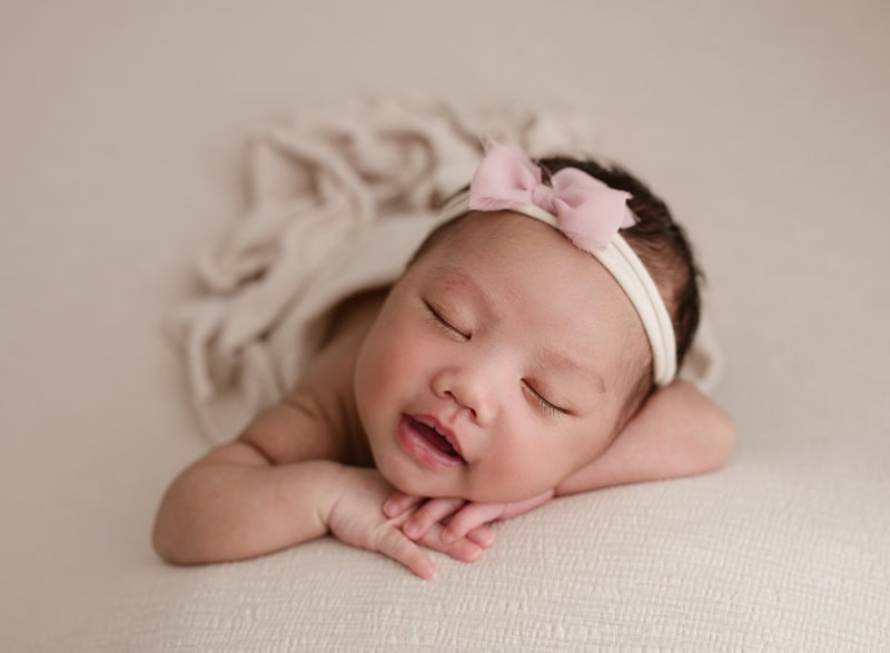 Adorable newborn girl peacefully sleeping with pink bow headband in calgary alberta