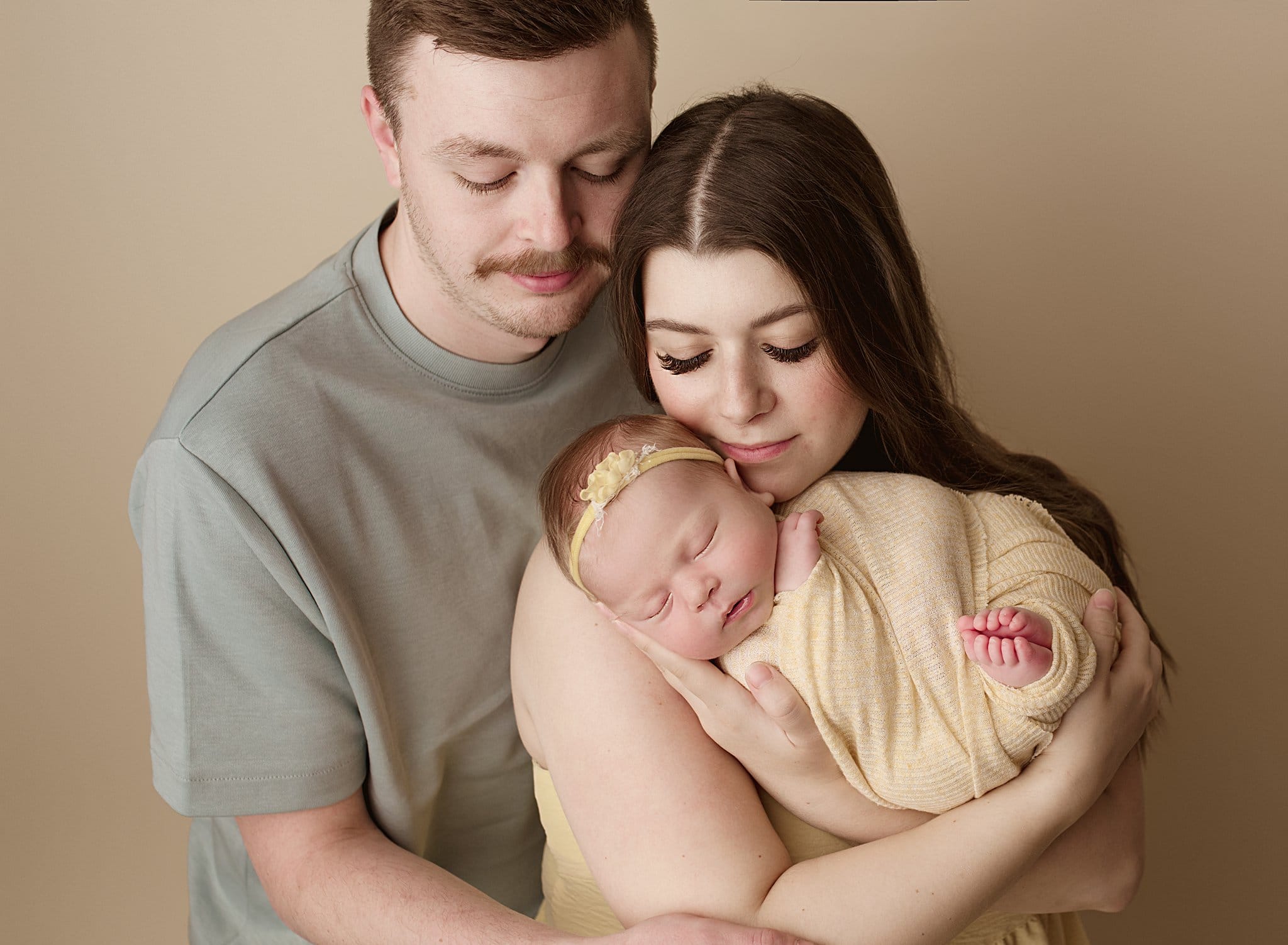 Heartwarming newborn family portrait with parents holding their sleeping baby girl.