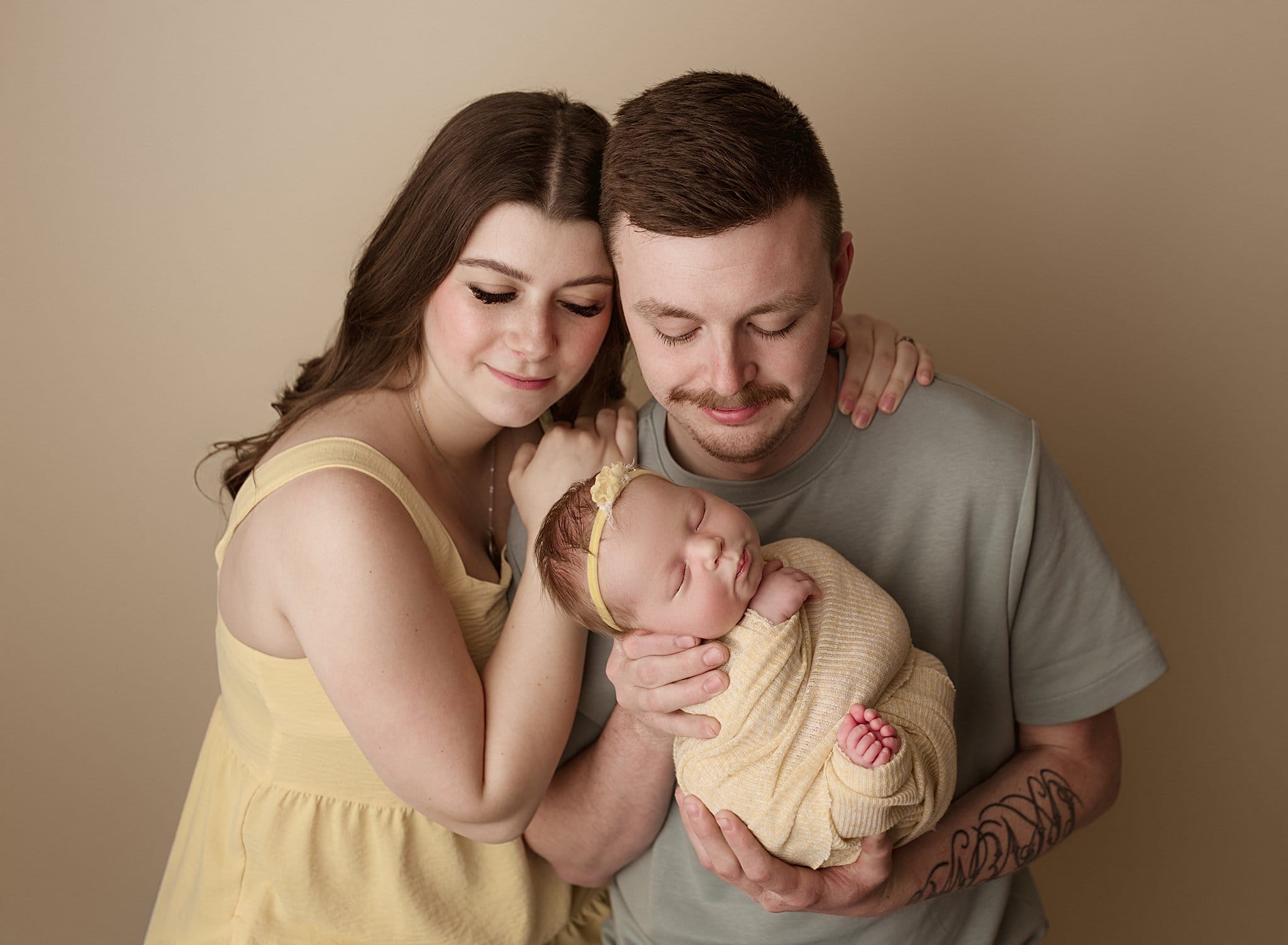 Newborn baby held by parents in a warm, intimate portrait.